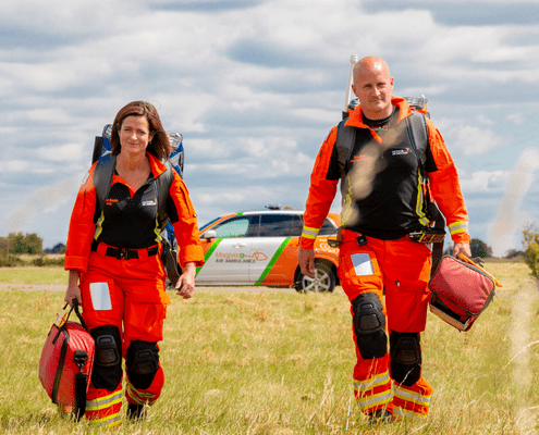 Paramedics walking with medical equipment in a field.
