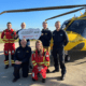 5 people who are receiving a cheque, with a helicopter behind