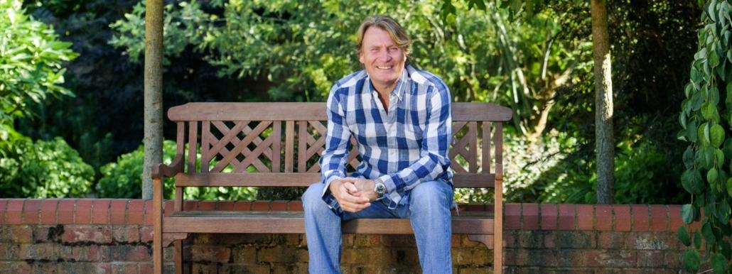 David Domoney sitting on a garden bench smiling.